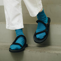 front of feet of person going down stairs wearing teal socks, black sandals, and white pants