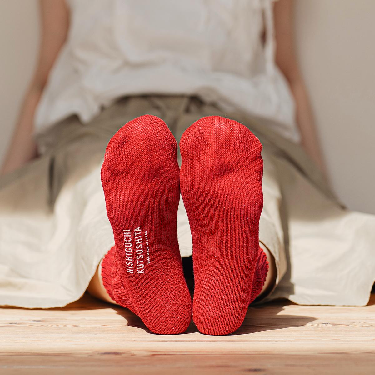 bottom of person's feet wearing red socks with visible brand name, sitting against a wall on the floor