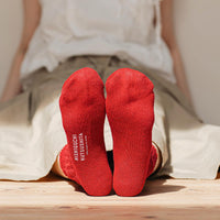 bottom of person's feet wearing red socks with visible brand name, sitting against a wall on the floor