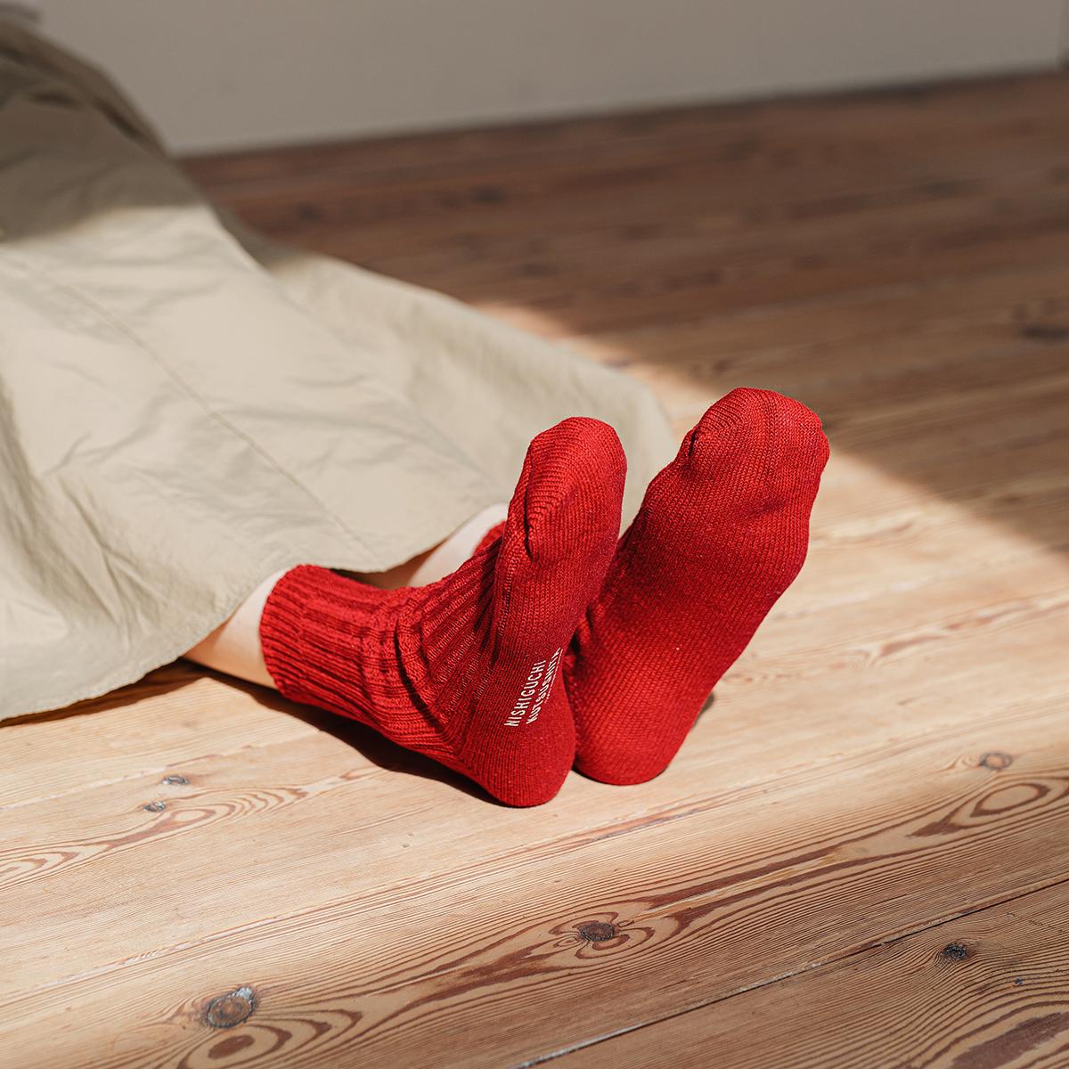 person sitting on a wood floor wearing red socks and a beige skirt