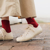 person wearing red socks and white sneakers standing on a brick surface