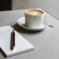 Cappuccino cup with saucer, pen, and notepad on a light surface