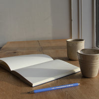 Open notebook with a pen and two ceramic cups on a wooden surface.