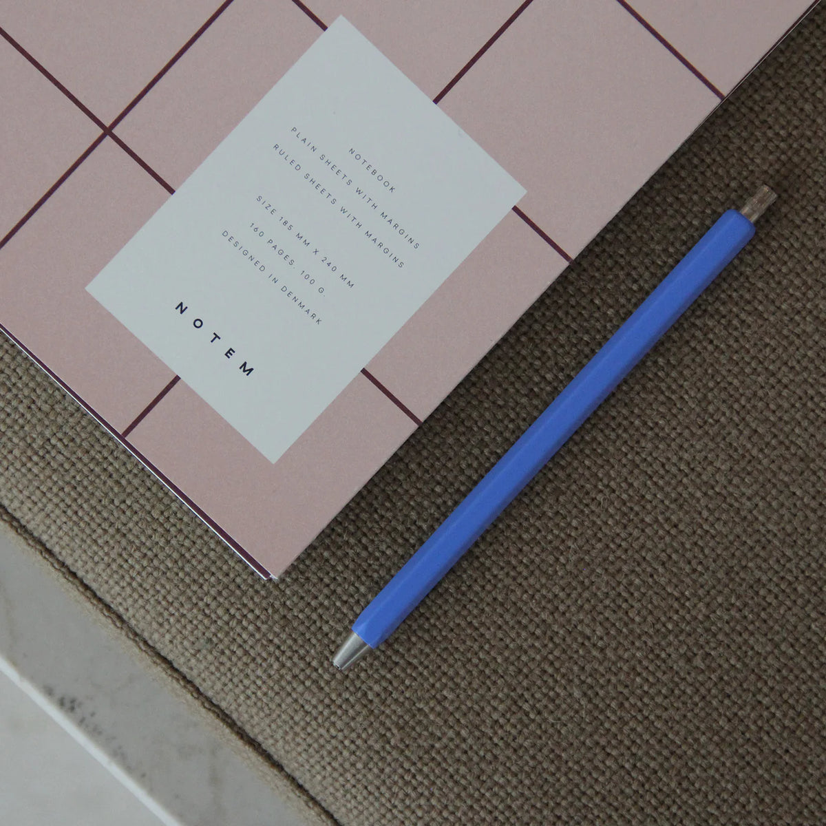 Pink notebook with a white label and blue pen on a textured surface
