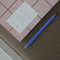 Pink notebook with a white label and blue pen on a textured surface