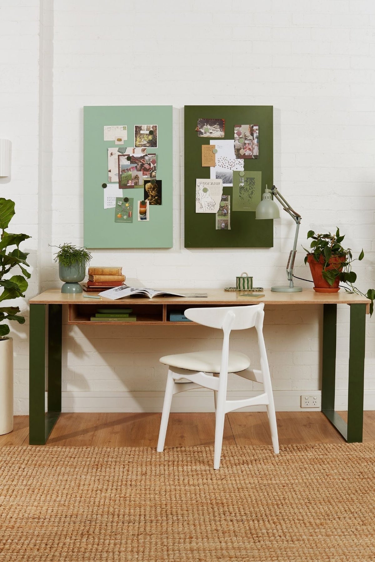 Home office with a wooden desk, white chair, and decorative display boards on a white wall.