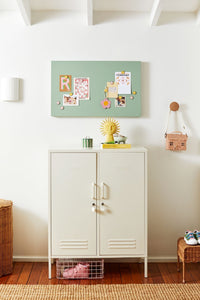 White locker cabinet with a green display board above it in a room with wooden flooring.