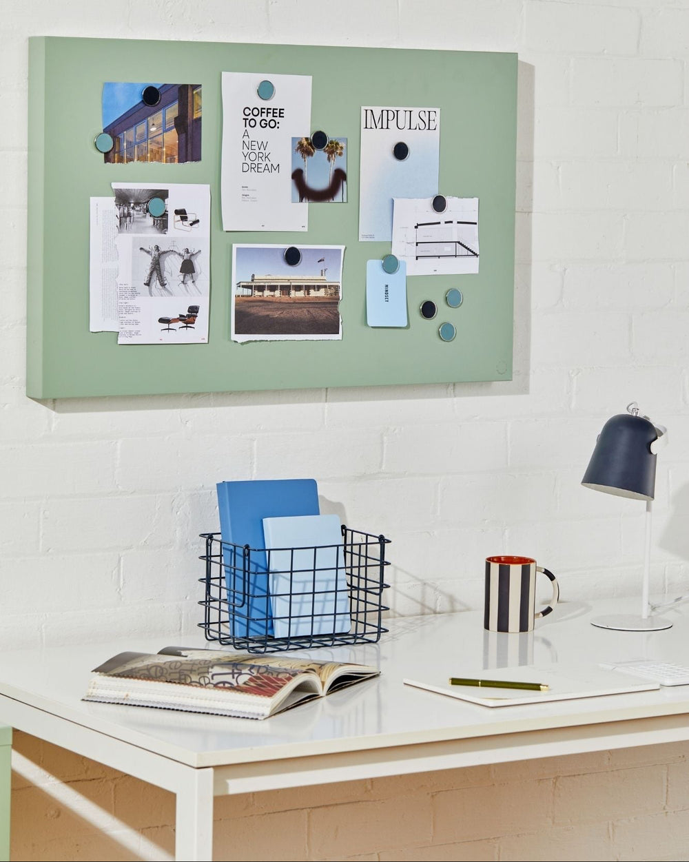 Green magnetic display board on a white wall above a desk with office supplies.