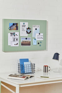 Green magnetic display board on a white wall above a desk with office supplies.