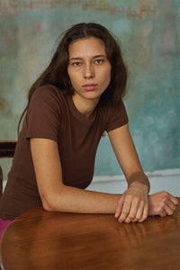 Woman in a brown shirt sitting at a table with a textured wall in the background