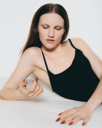 Woman in a black tank top examining her painted nails against a white background
