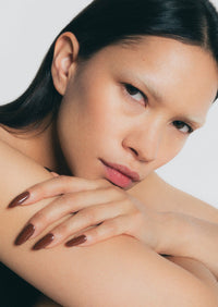 Close-up of a woman with dark hair and brown nail polish on a white background