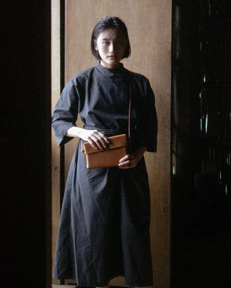 Woman in a dark dress holding a brown bag against a neutral background