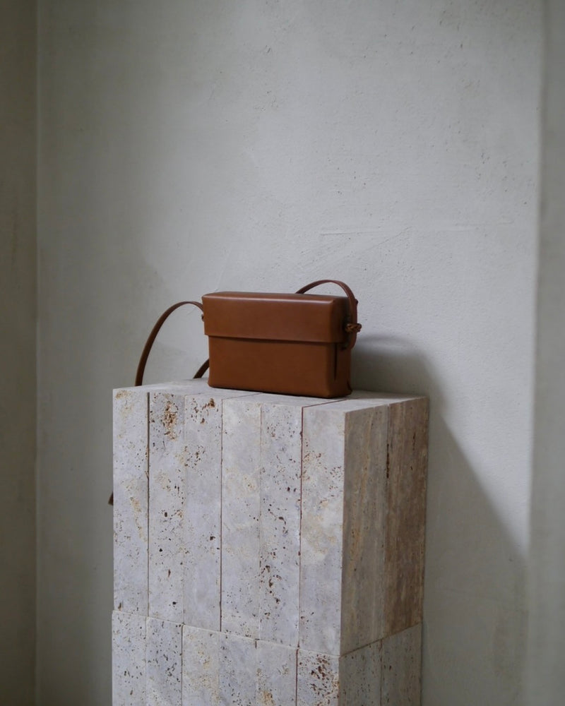 Brown leather bag on a textured stone block against a plain wall