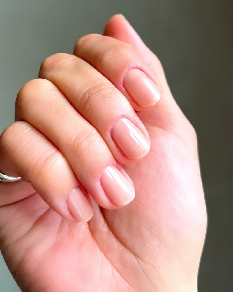 Person's hand with fingers curled showing sheer painted fingernails on a dark green background