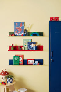 Children's bookshelves with books and toys against a yellow wall, next to a blue locker.