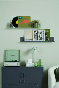 Vinyl records and a record player with shelves against a light green wall.