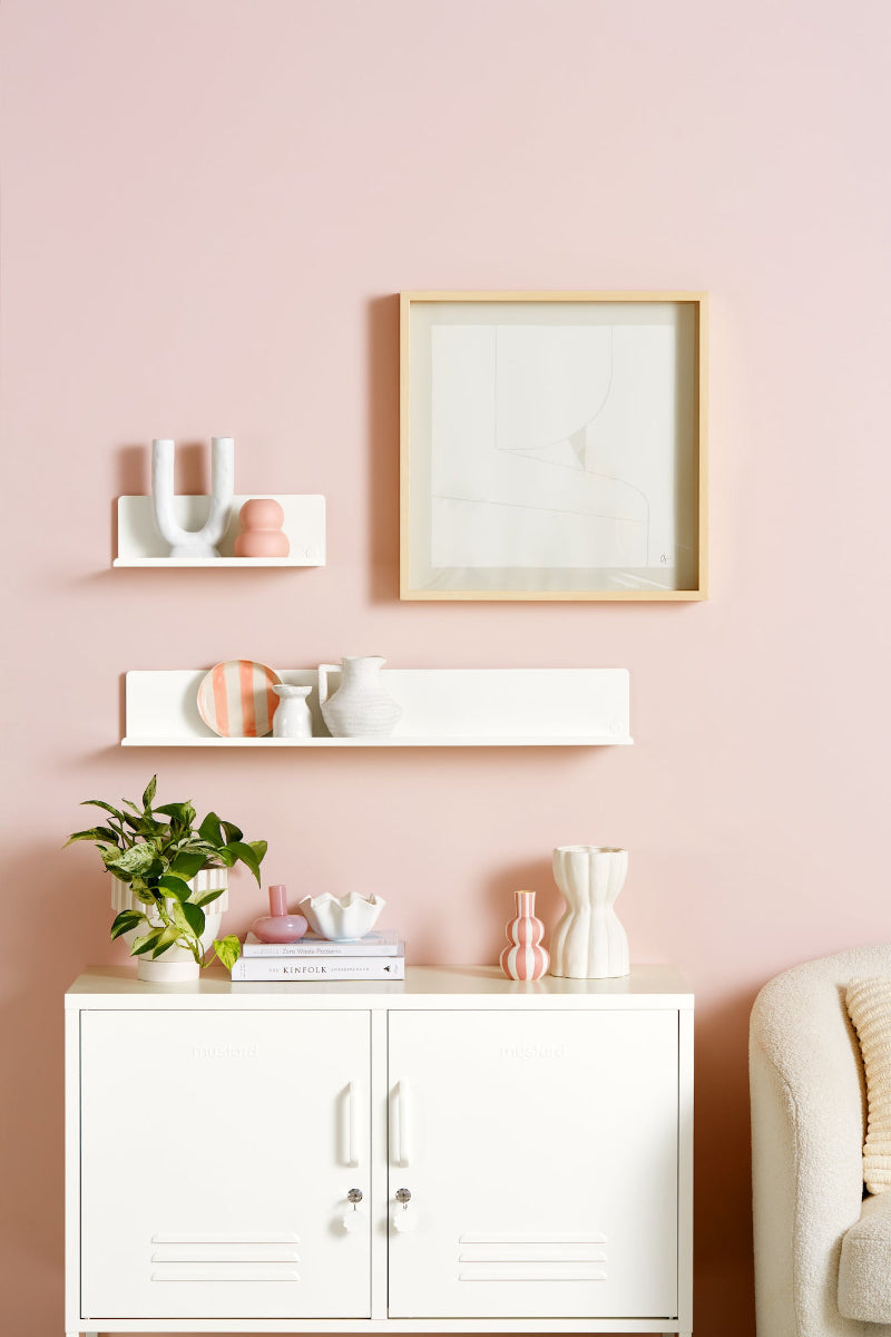 White cabinet with decorative items on shelves against a pink wall