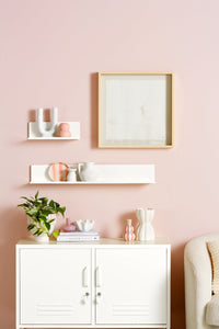 White cabinet with decorative items on shelves against a pink wall
