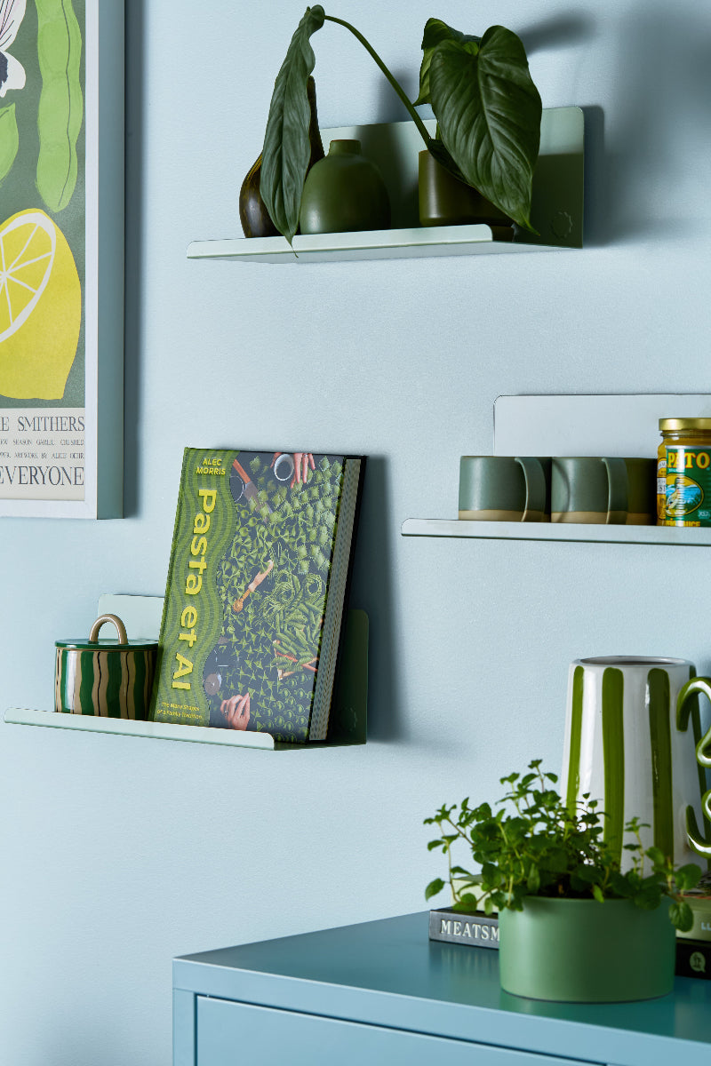 Shelves with green plants, books, and kitchenware against a light blue wall.