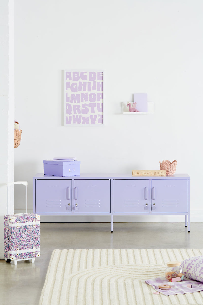Light purple sideboard in a room with a white wall and a rug on the floor.
