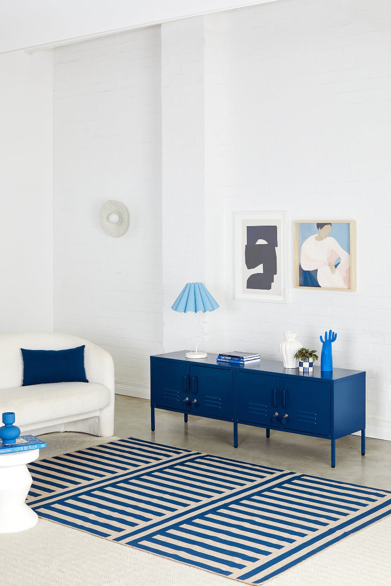 Modern living room with blue and white decor, including a rug, sideboard, and lamp.
