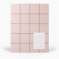 Pink grid-patterned journal with a white card on a white background