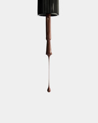 Brown nail polish being dripped from a brush onto a white background