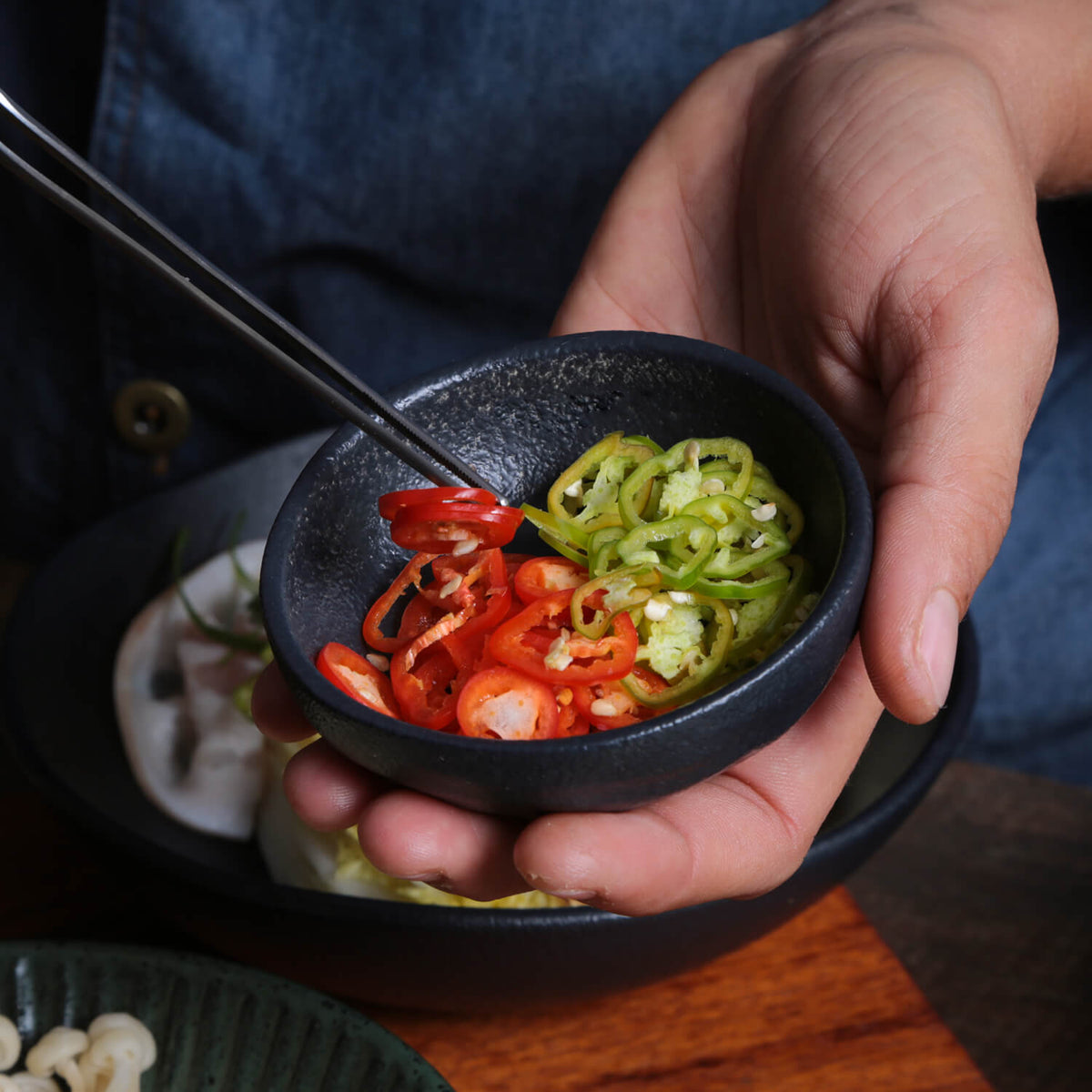 Person holding a small black ramekin with sliced red and green peppers.