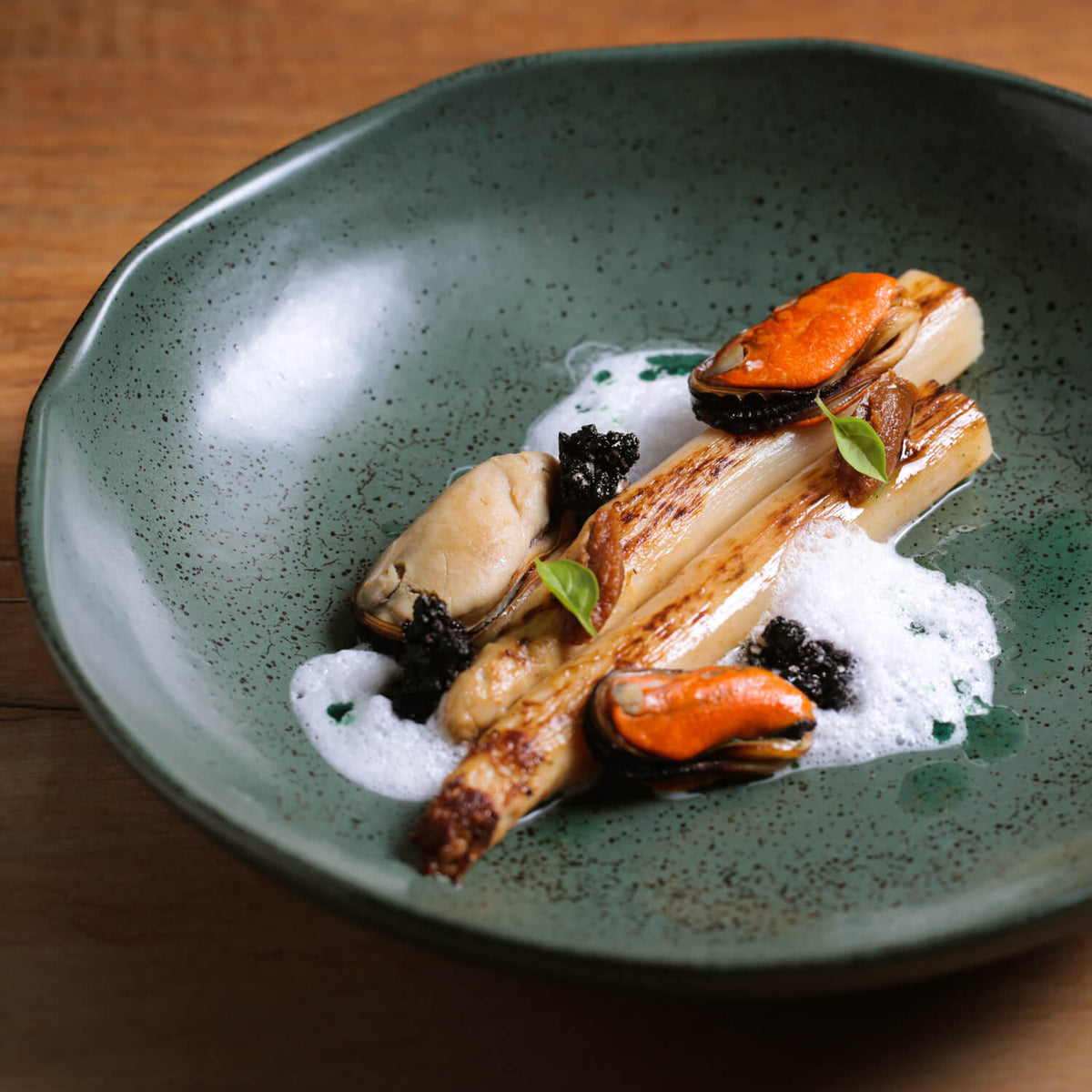 Gourmet dish with seafood and vegetables on a green ceramic plate.