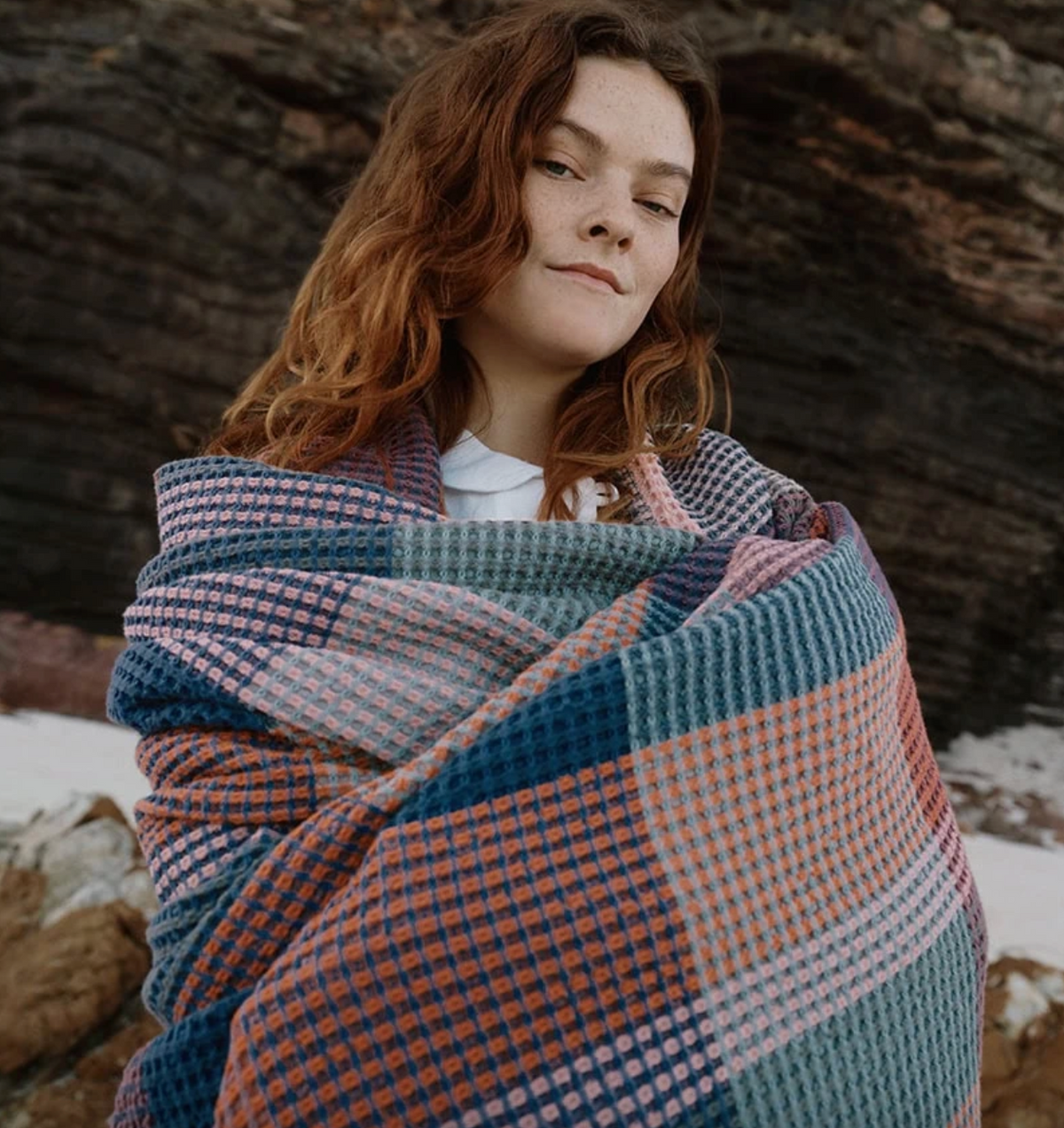 Woman wrapped in a colorful plaid blanket against a natural background