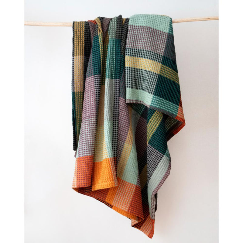 A multicolor plaid waffle-weave throw blanket draped over a light wooden dowel against a plain white background.