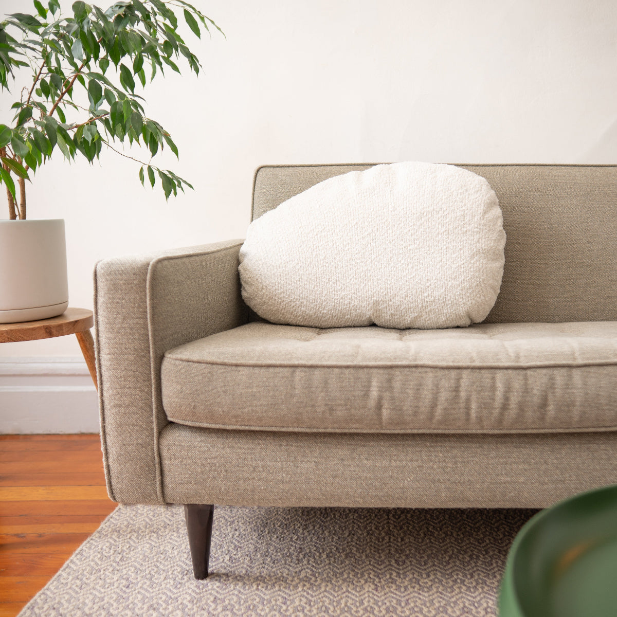 Beige sofa with a white cushion in a room with a plant and wooden floor.