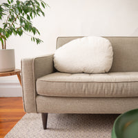 Beige sofa with a white cushion in a room with a plant and wooden floor.