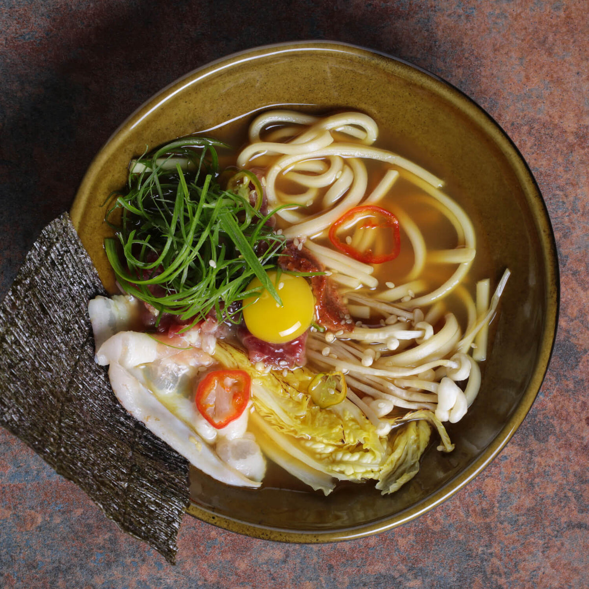 Bowl of ramen with various toppings on a dark surface
