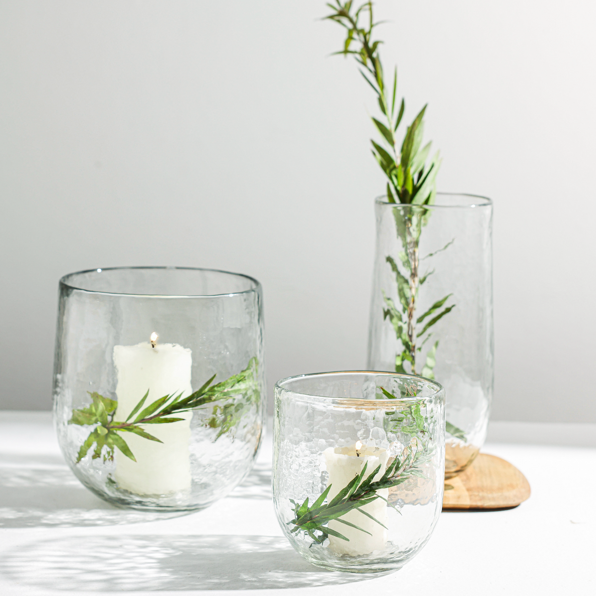 Clear glass vessels with candles and greenery on a light surface.