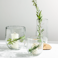 Clear glass vessels with candles and greenery on a light surface.