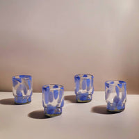 Four blue and white glass tumblers on a plain surface with a neutral background