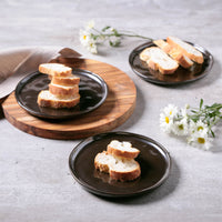 Bread slices on black plates with a wooden cutting board and flowers on a gray surface