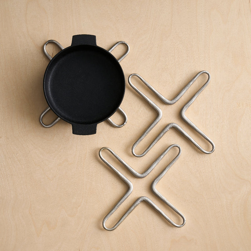 Pewter Trivets and a black pot on a wooden surface