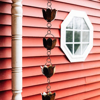 Decorative metal rain chain hanging in front of red siding and a hexagon window.