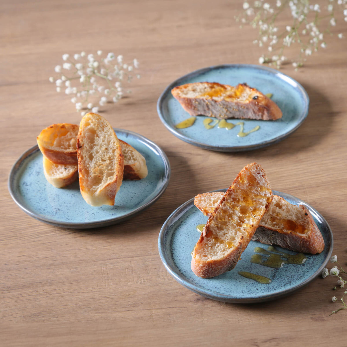Three blue plates with slices of bread on a wooden surface with white flowers.