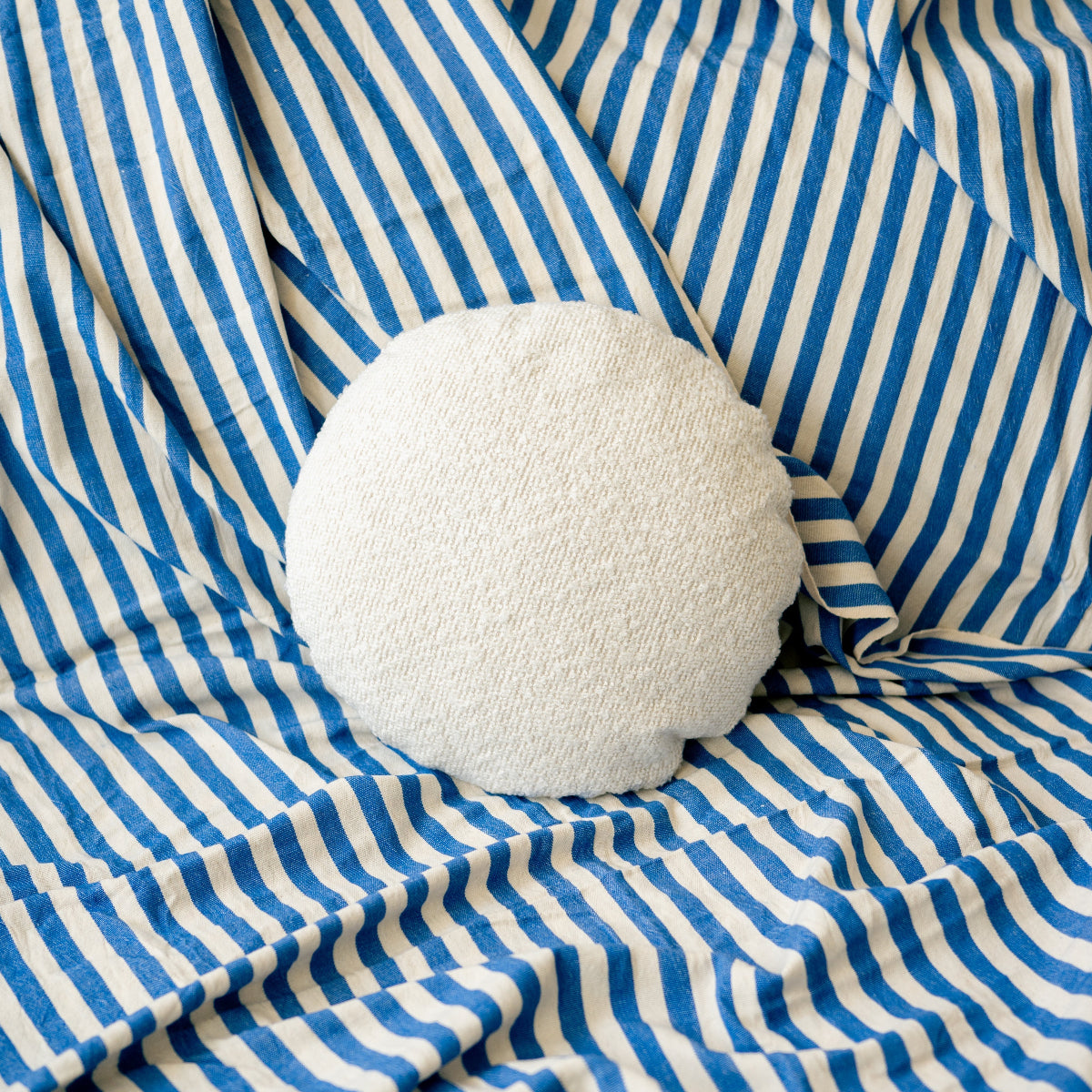 White textured round pillow on blue and white striped fabric