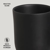 Black ceramic cup with 'Reactive Glaze' text and 'Each product is unique' label on a light gray background