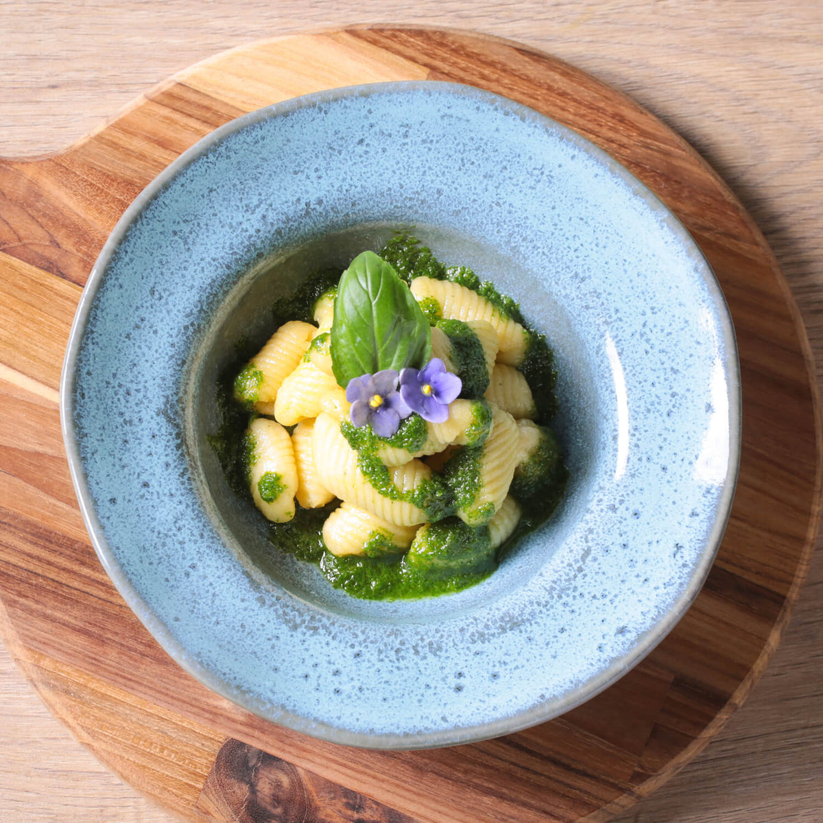 Blue bowl with pasta and green sauce on a wooden board