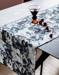 Table runner with black and white abstract pattern on a table with a glass of red wine and berries.