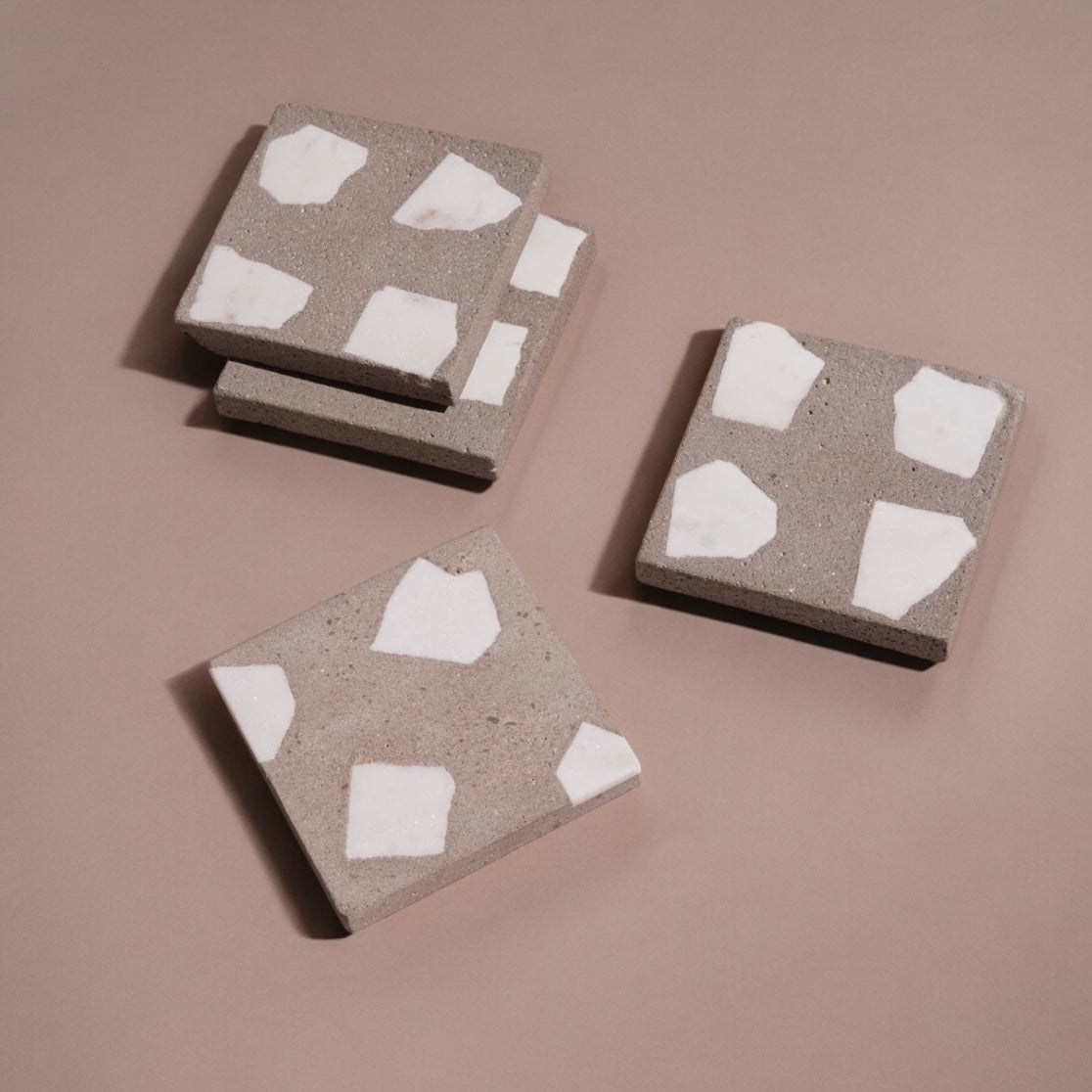 Four square concrete coasters with white abstract patterns on a brown background