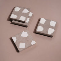 Four square concrete coasters with white abstract patterns on a brown background