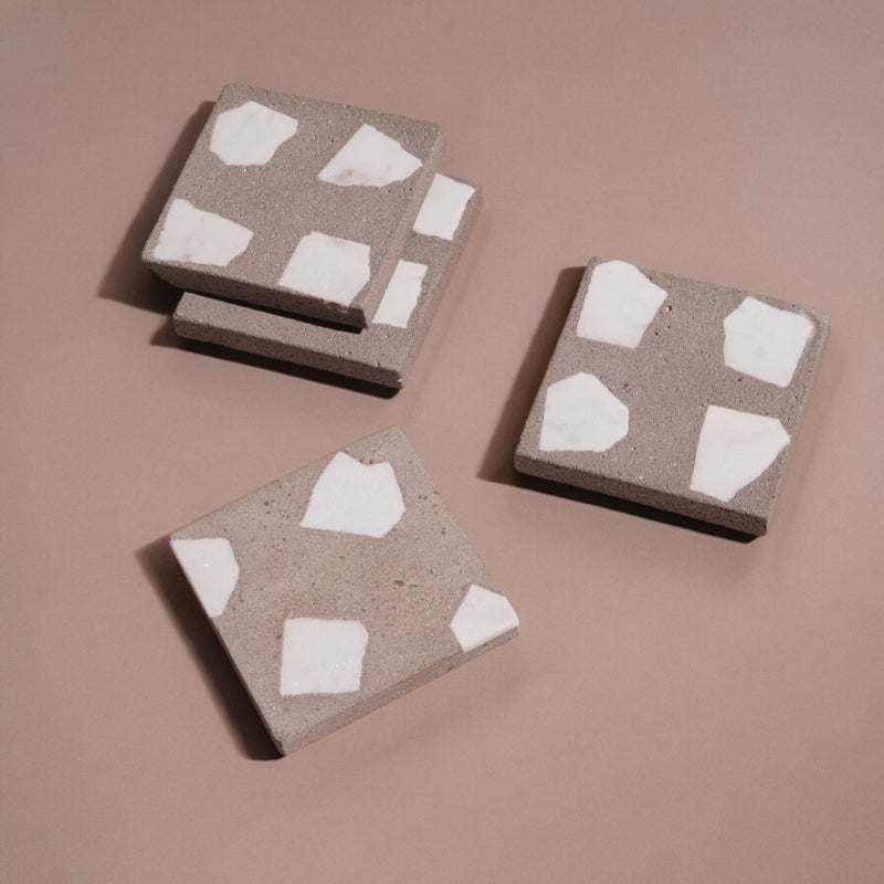 Four square concrete coasters with white abstract patterns on a brown background