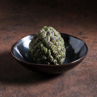 Green textured fruit like object in a dark ceramic bowl on a dark brown surface